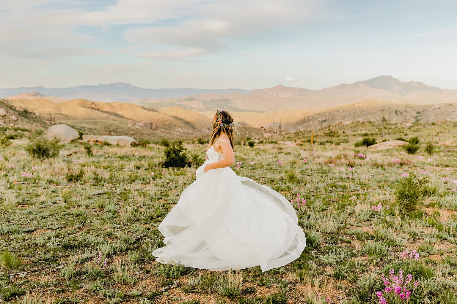 bride twirling in wedding dress among wildflowers and Colorado mountains