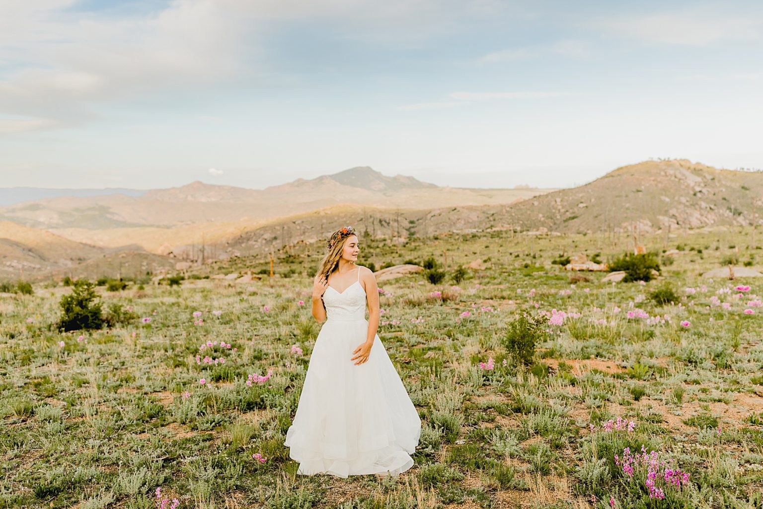 bride in wedding dress among wildflowers and Colorado mountains