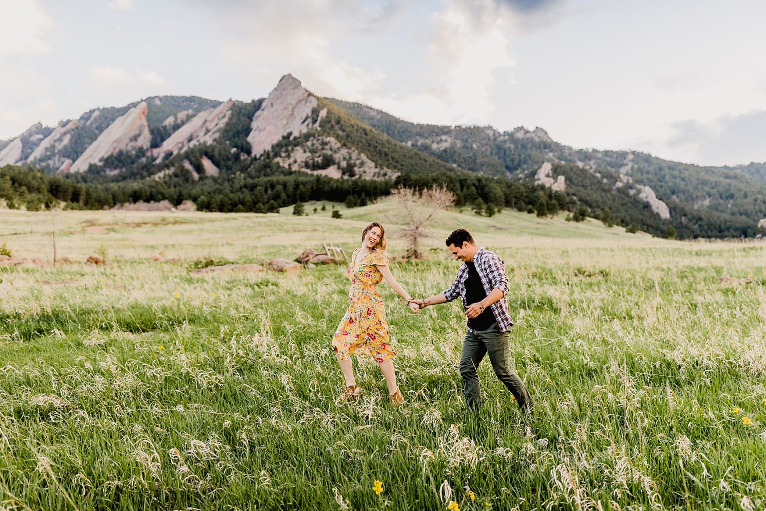 adventurous couple running together at chautauqua park in boulder colorado for their mountain engagement photos including beautiful green scenery