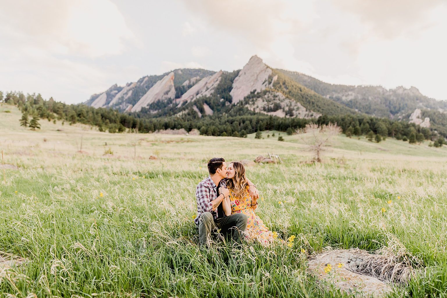 adorable couple sitting in grass at chautauqua park in boulder colorado for their summer engagement photos