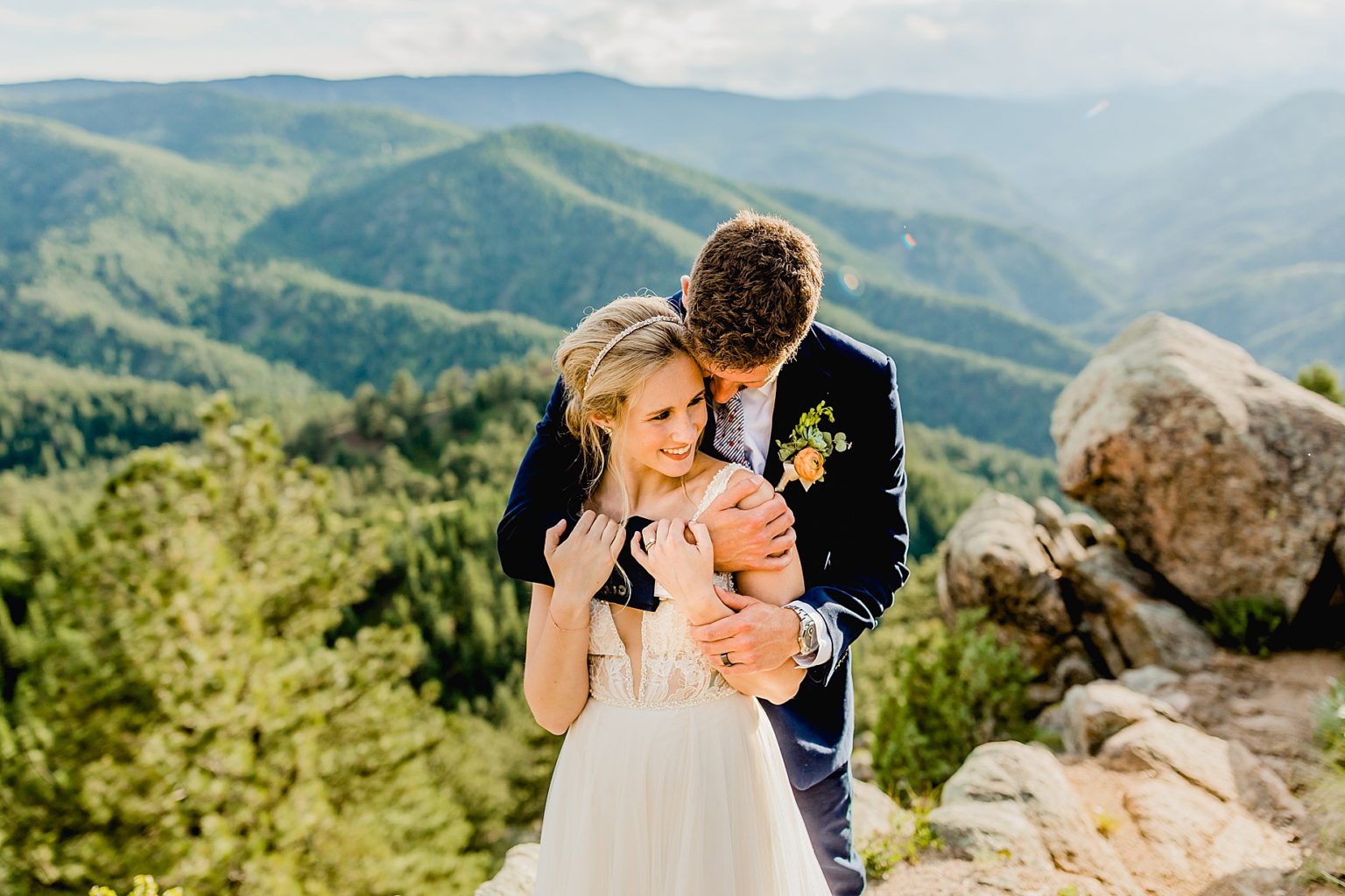 groom hugs bride from behind with incredible mountain background of boulder colorado