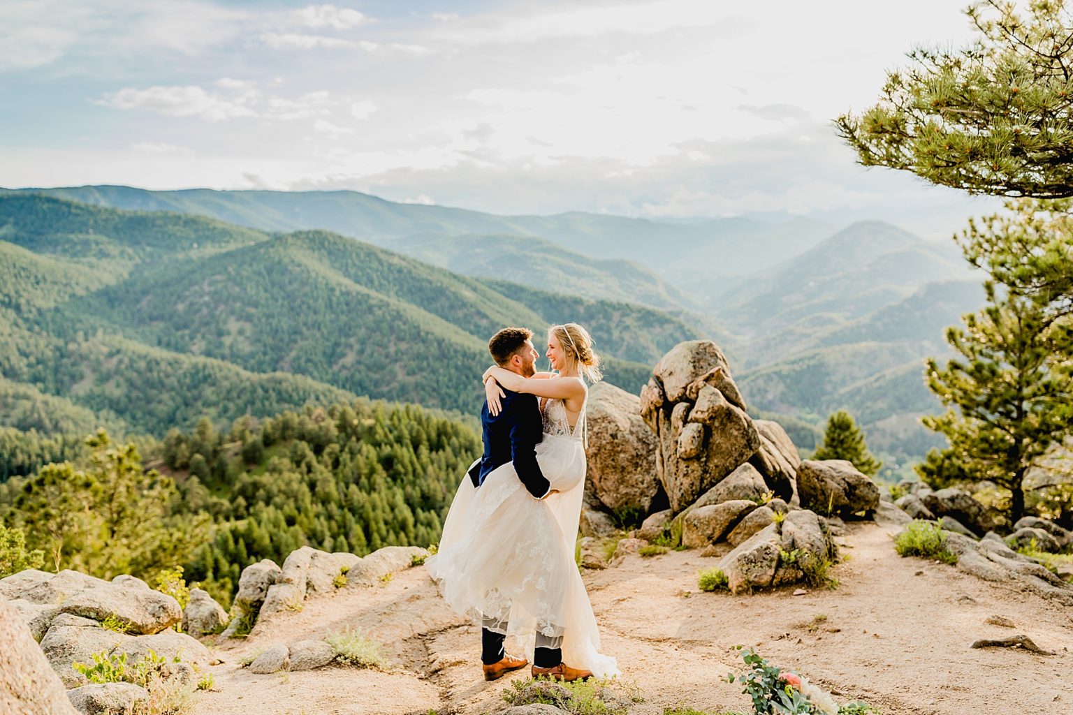 bride and groom embrace with stunning green mountain background of colorado mountains and trees