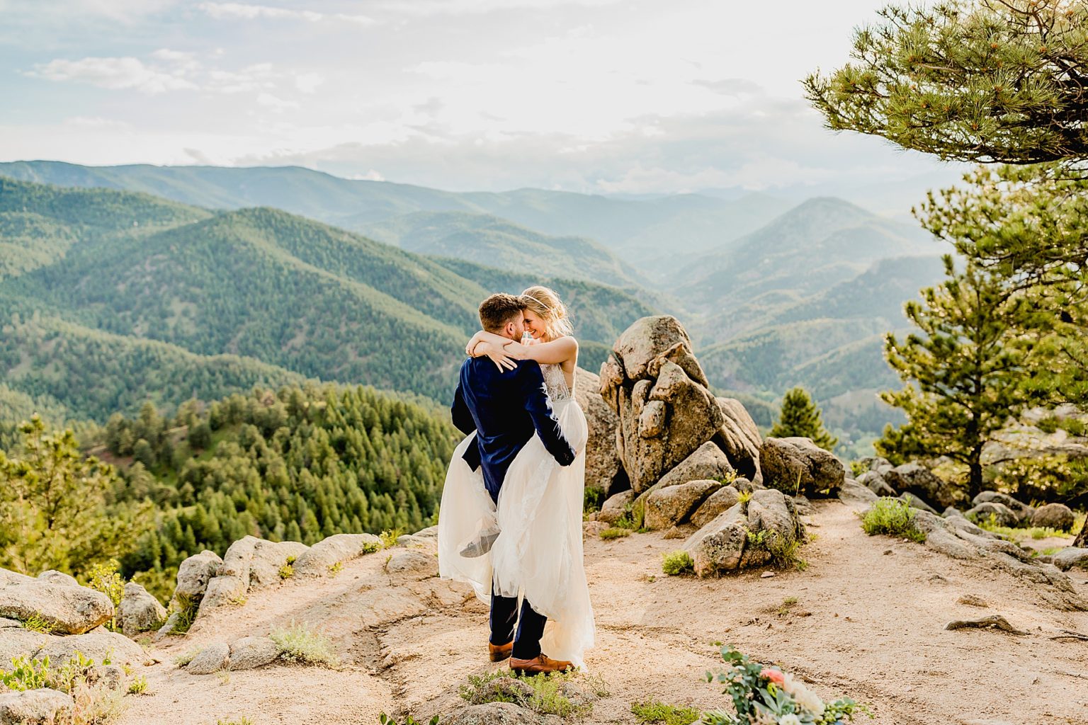 bride and groom embrace with stunning green mountain background of colorado mountains and trees