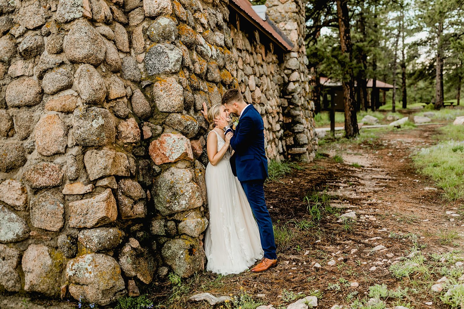 couple standing against stone shelter on flagstaff mountain and hugging one another
