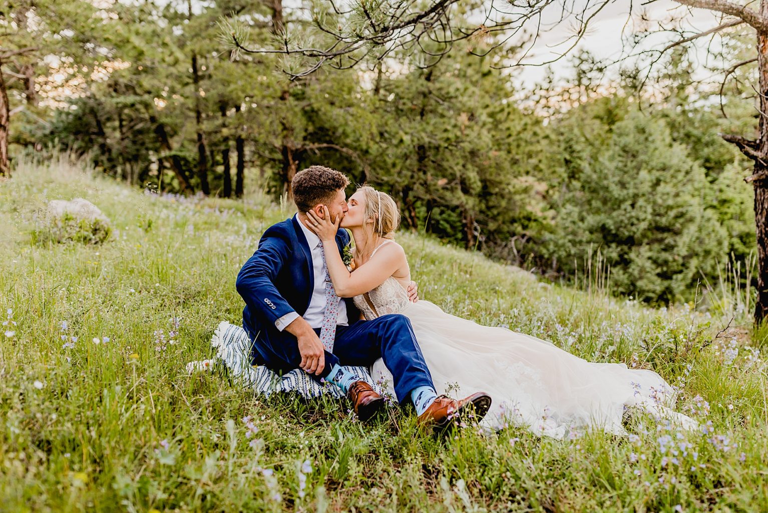 bride and groom are cuddling in the wildflowers for their elopement with trees in the background