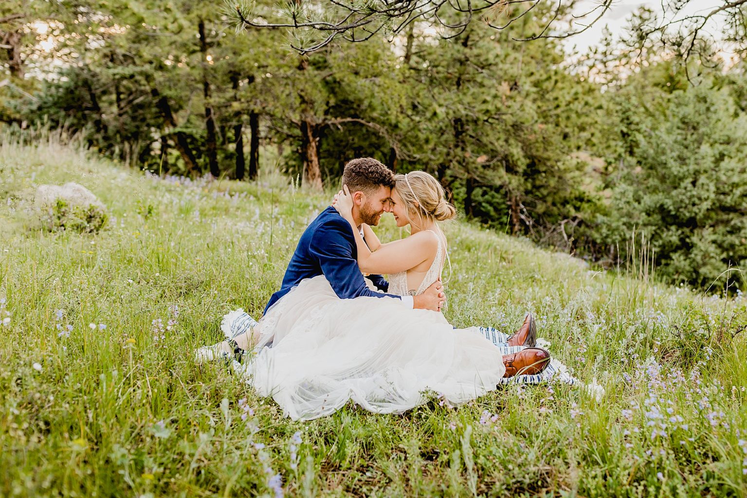 bride and groom embrace together while sitting in the wildflowers of boulder colorado for their wedding