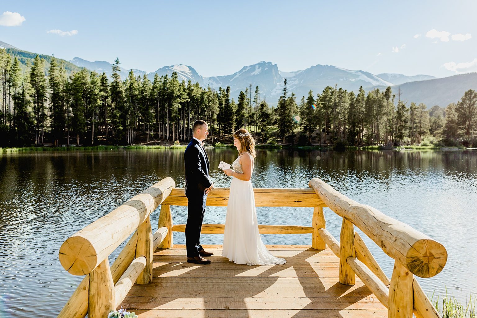 bride and groom exchange vows Sprague Lake in Rocky Mountain national park on a beautiful summer day with gorgeous mountain views in the background