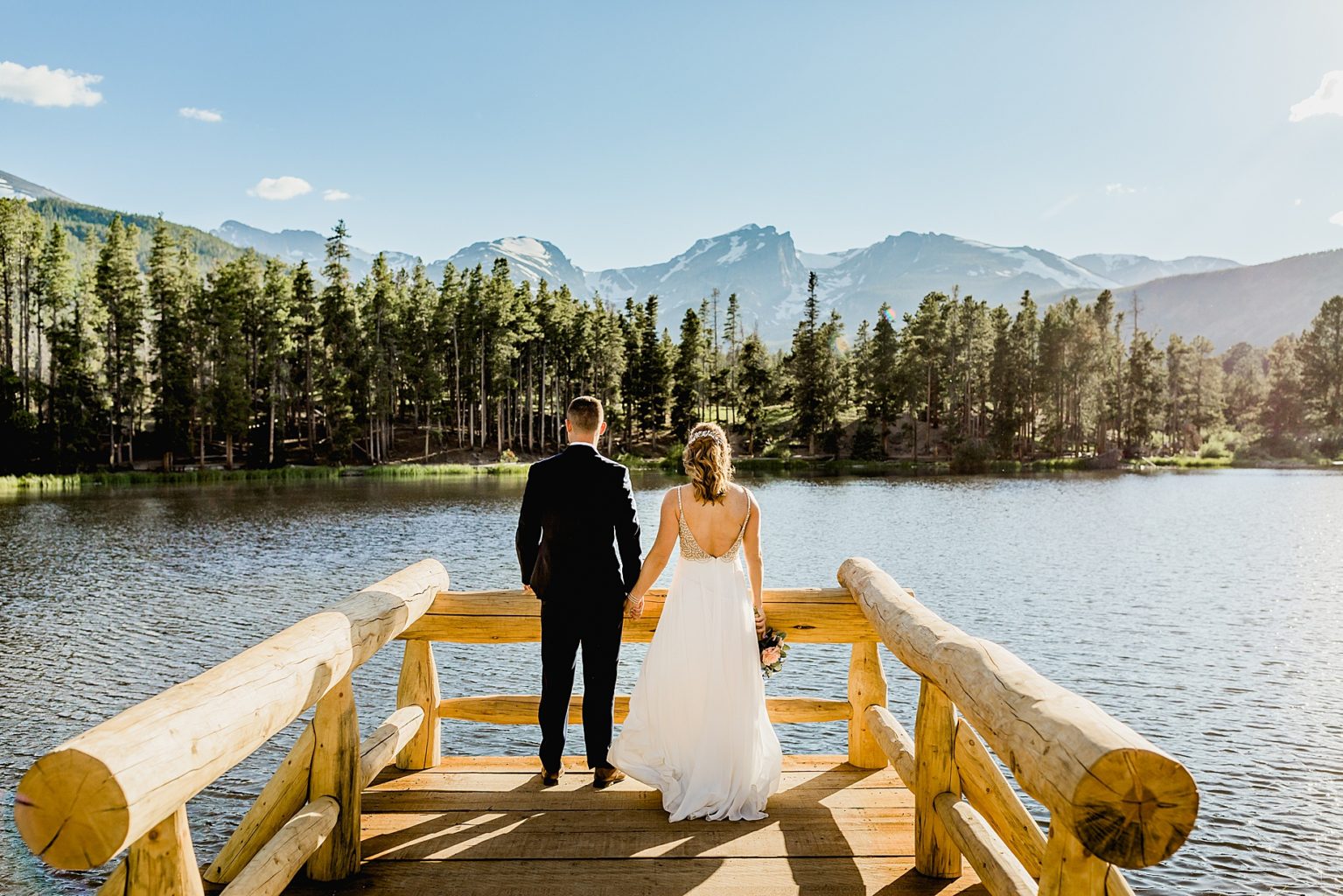 bride and groom hold hands after elopement ceremony at Sprague Lake with beautiful mountain and lake scenery