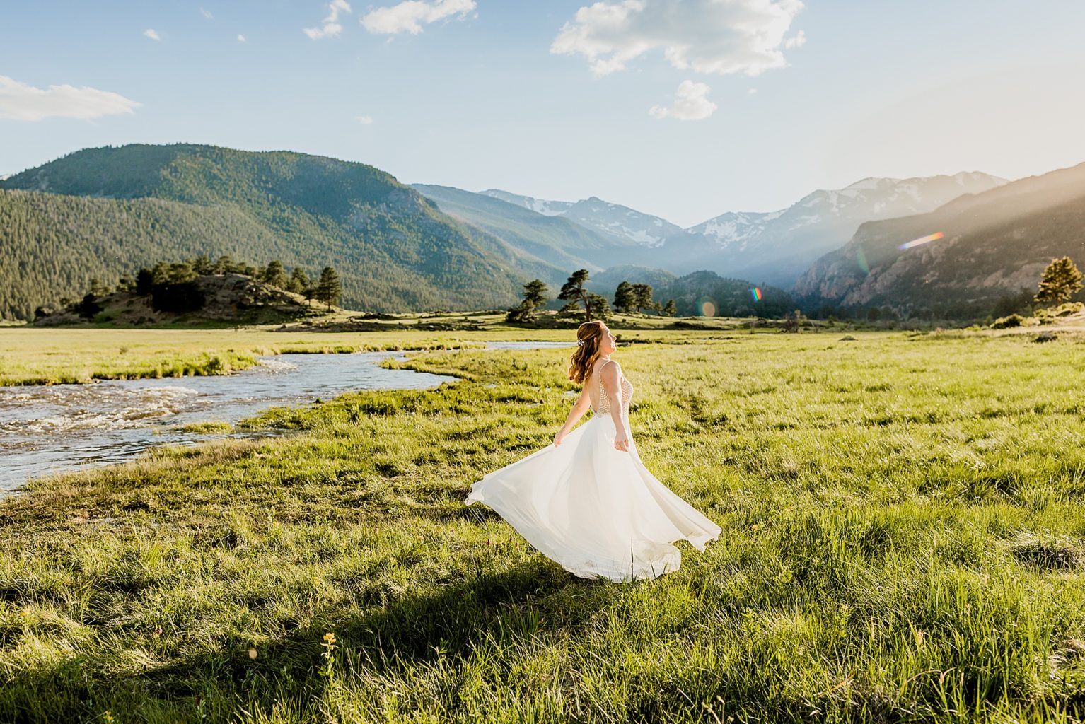 bride stands in colorado meadow in Estes Park with gorgeous blue mountain background and green grass