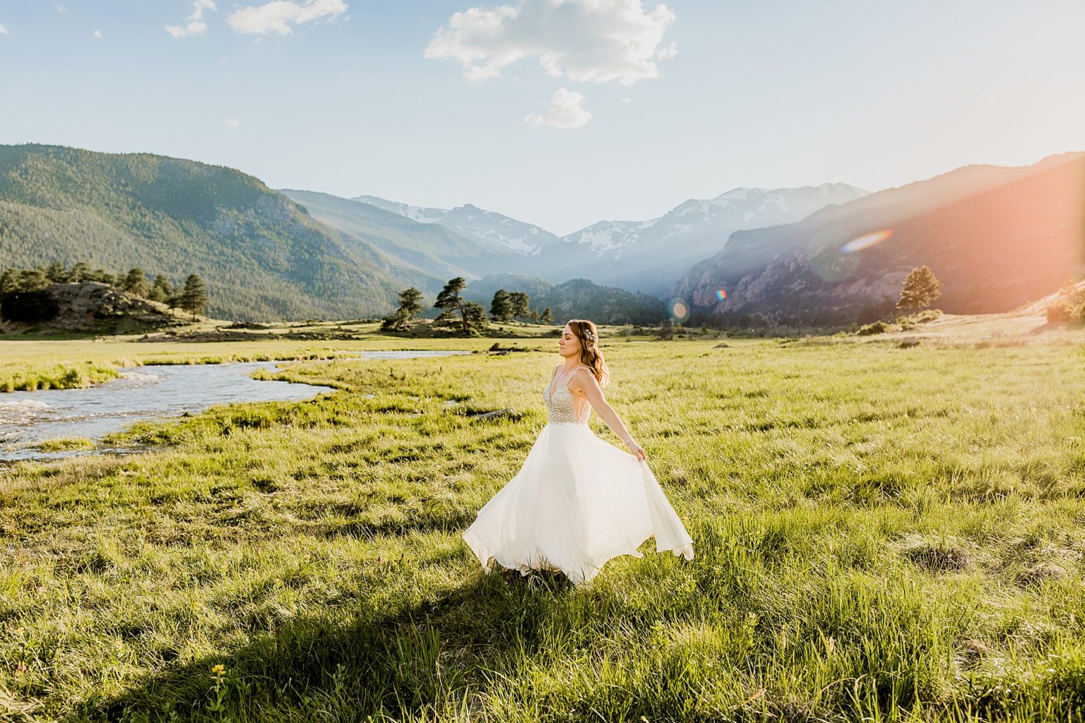 bride stands in colorado meadow in Estes Park with gorgeous blue mountain background and green grass