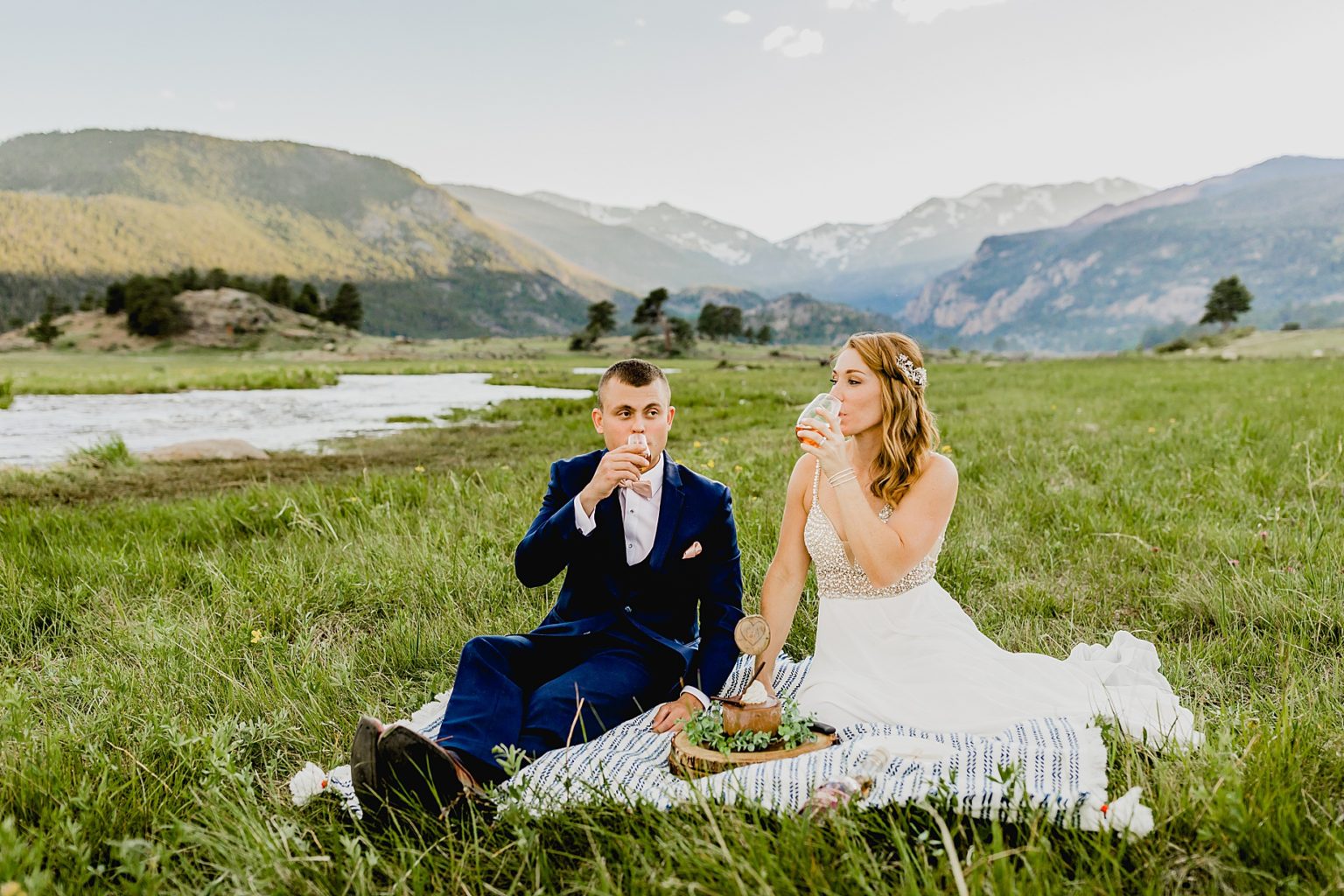 bride and groom share drinks in Estes Park while sitting in grass