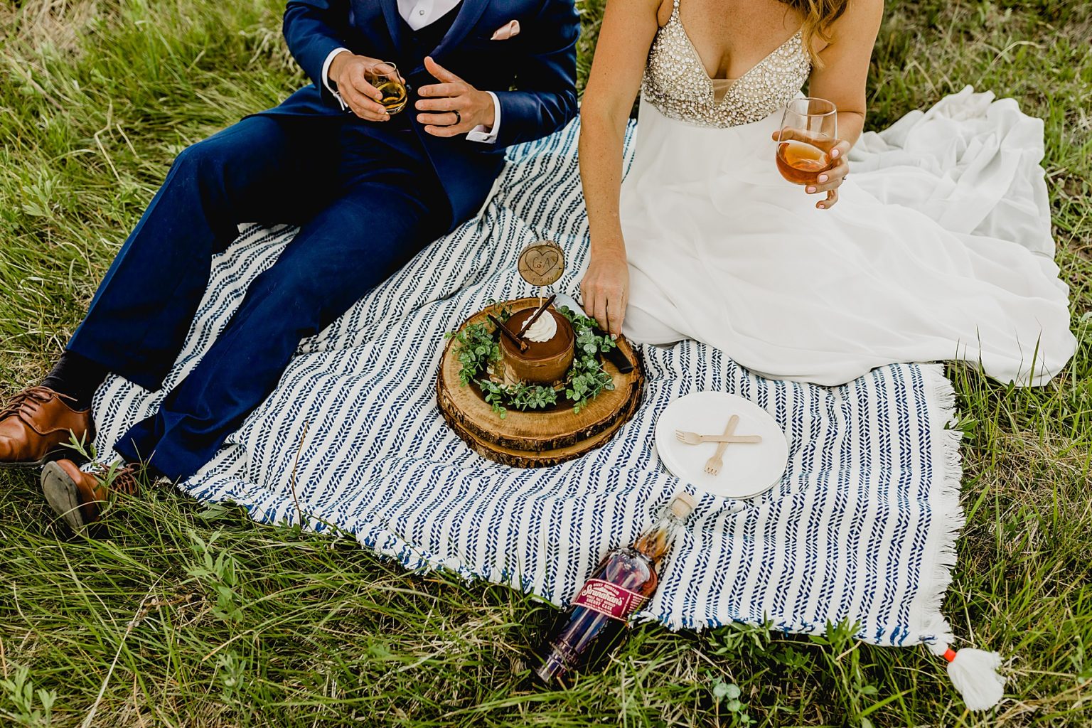 bride and groom share drinks in Estes Park while sitting in grass