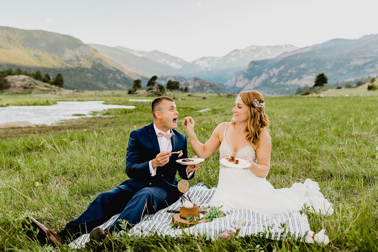 bride and groom eat wedding cake with mountain backdrop