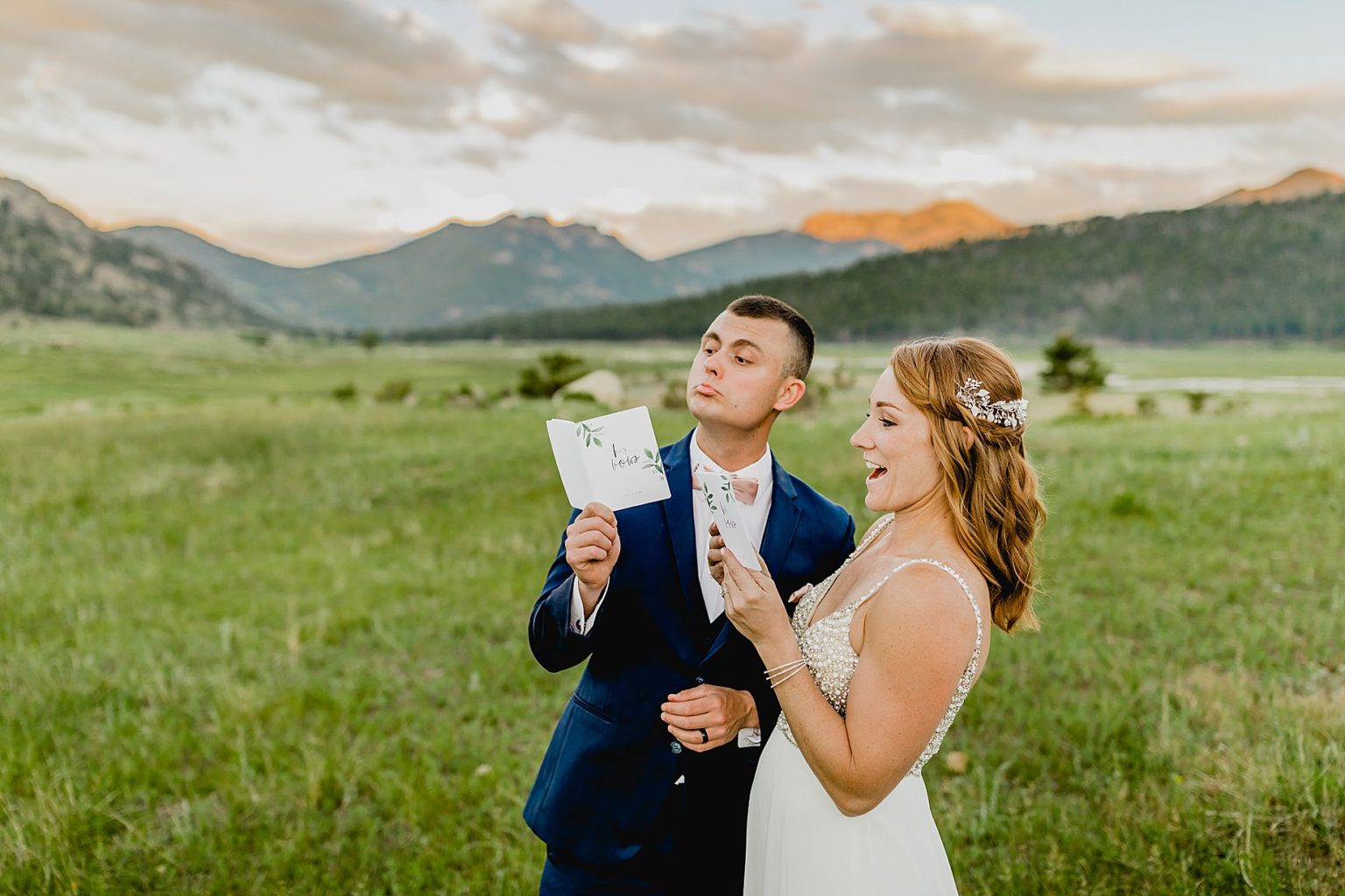bride and groom look at vow books with mountain background