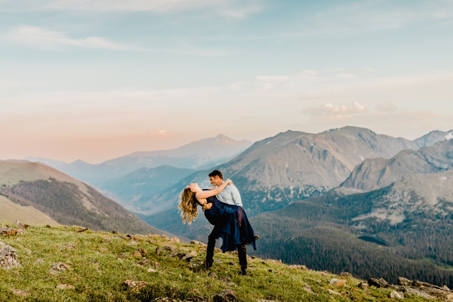 man lifts and dips woman for a kiss on the neck with gorgeous pink sunset and mountain scenery in the backdrop
