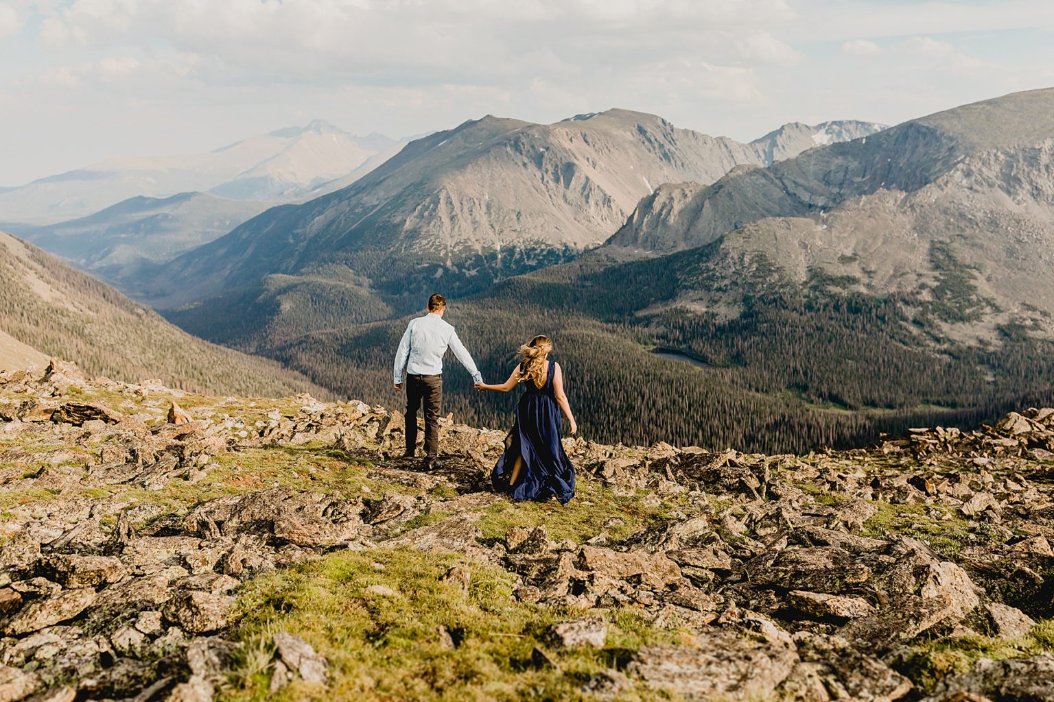 couple holding hands walking over rocky terrain with a beautiful colorado mountain backdrop
