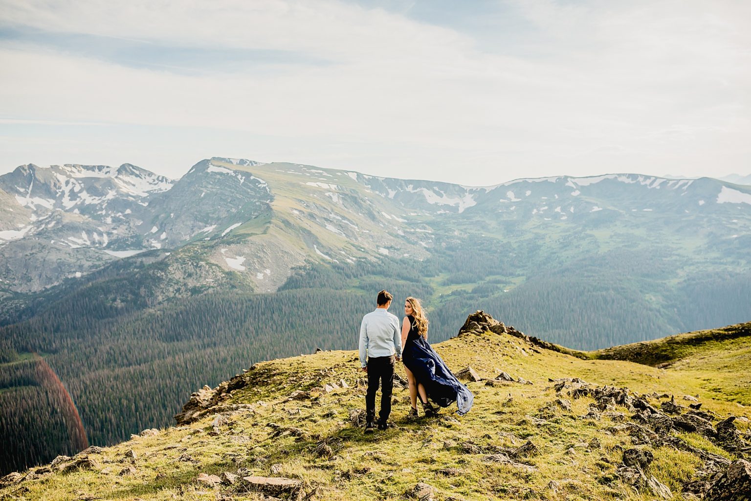 couple holding hands walking over rocky terrain with a beautiful colorado mountain backdrop