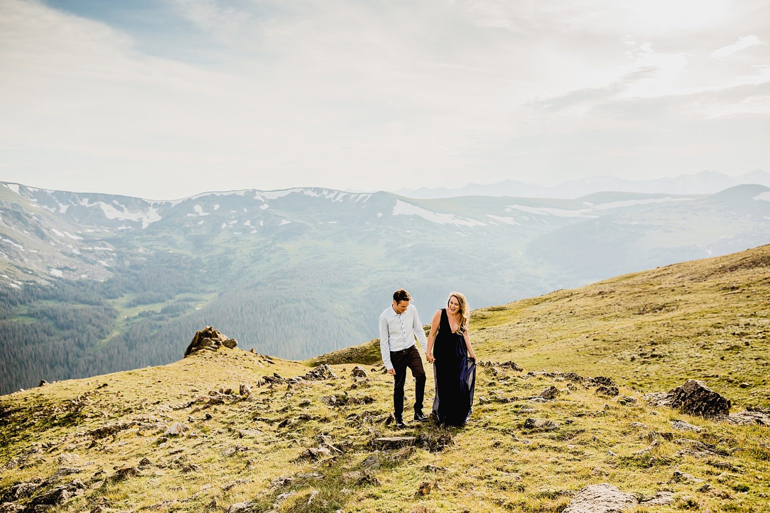 couple holding hands and laughing while walking over rocky terrain with a beautiful colorado mountain backdrop