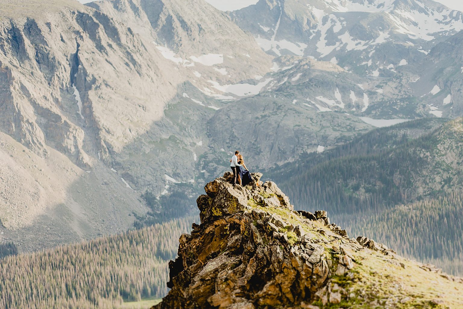 couple embraces on Rocky Mountain cliff edge with gorgeous mountain scenery in the background