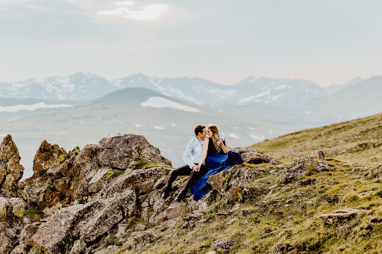 couple sits on mountain edge with beautiful colors and background