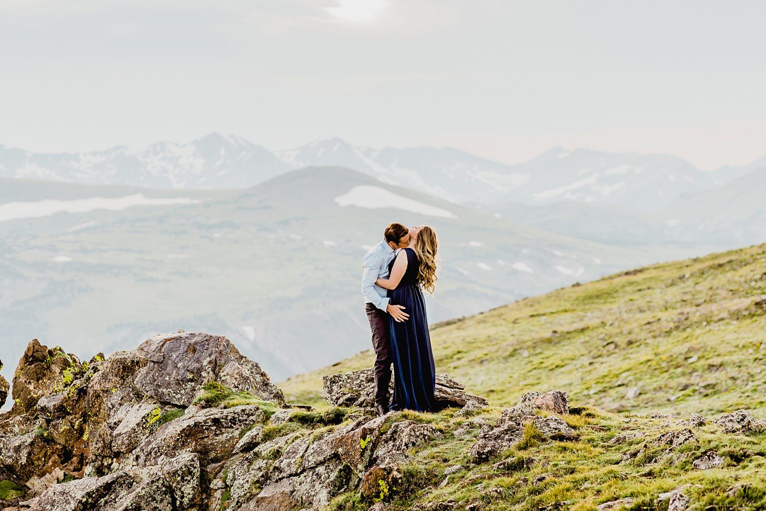 couple hugs one another overlooking the incredible Rocky Mountains and pink sunset