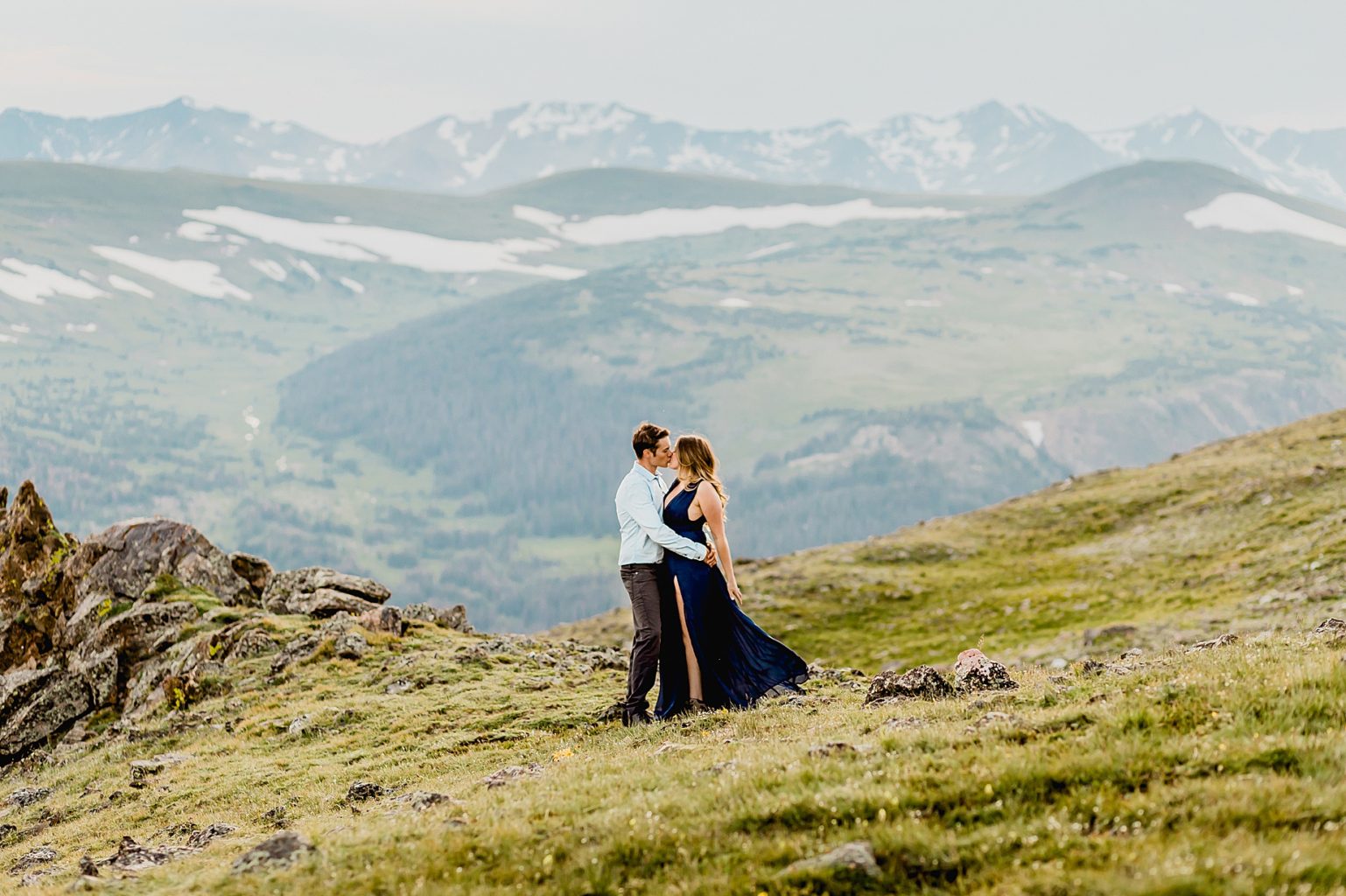 couple hugs each other among the grass and yellow wildflowers with stunning Rocky Mountain background