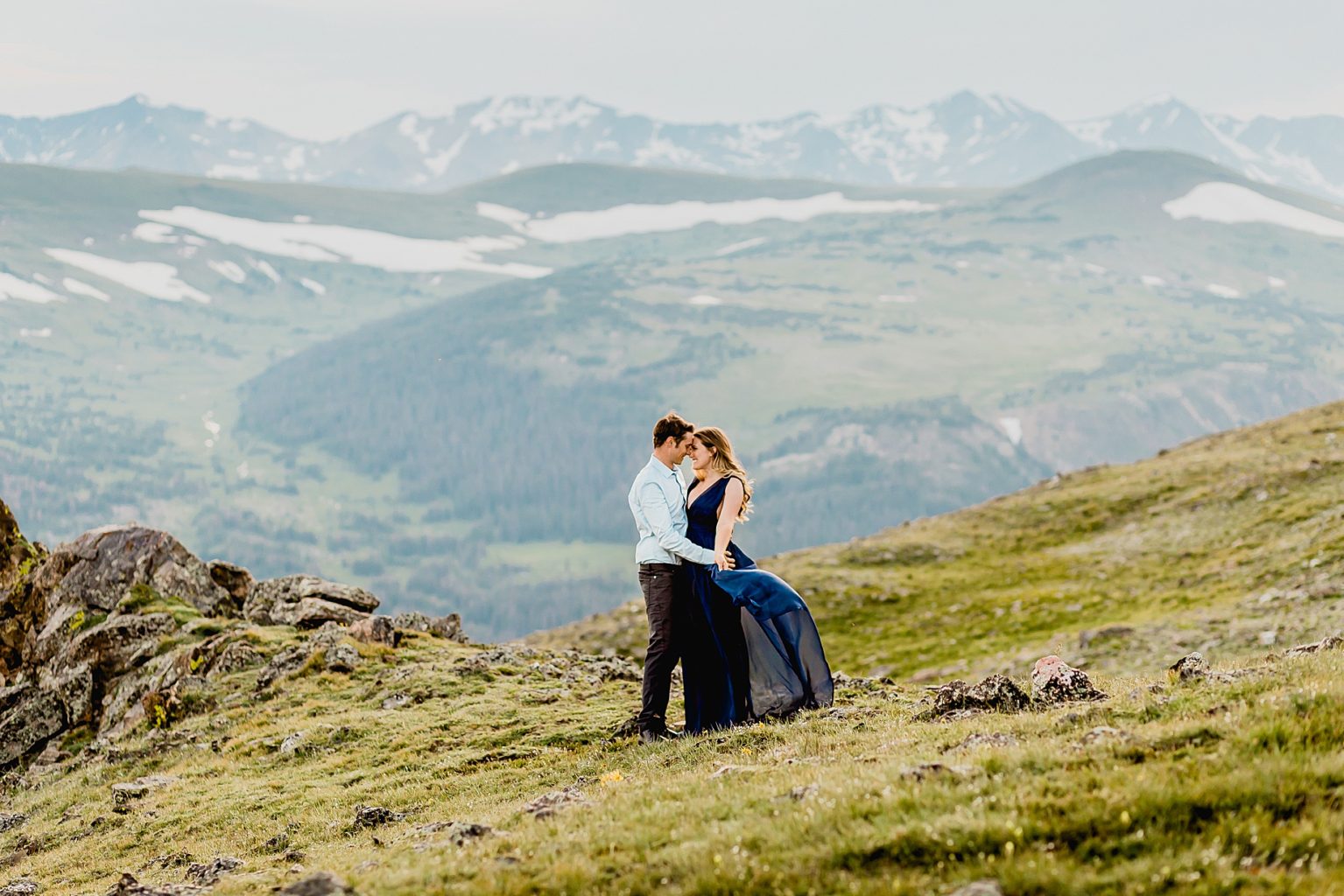 couple hugs each other among the grass and yellow wildflowers with stunning Rocky Mountain background