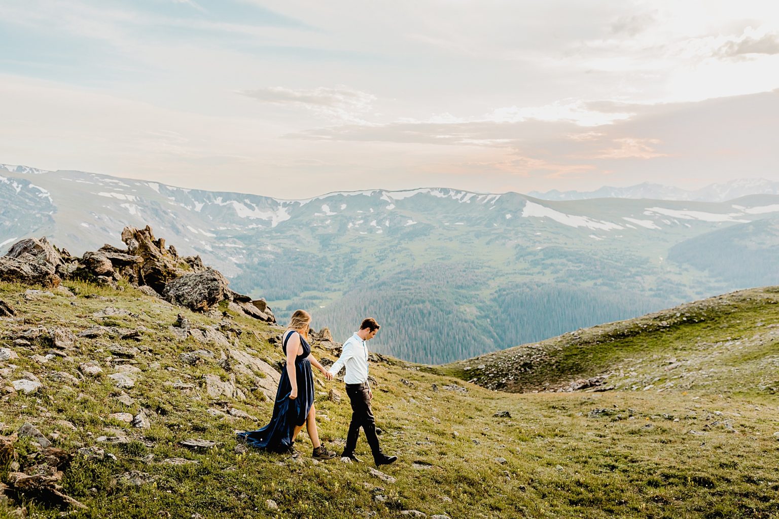 couple hiking down mountain together in their nice attire and hiking shoes with gorgeous mountain backdrop
