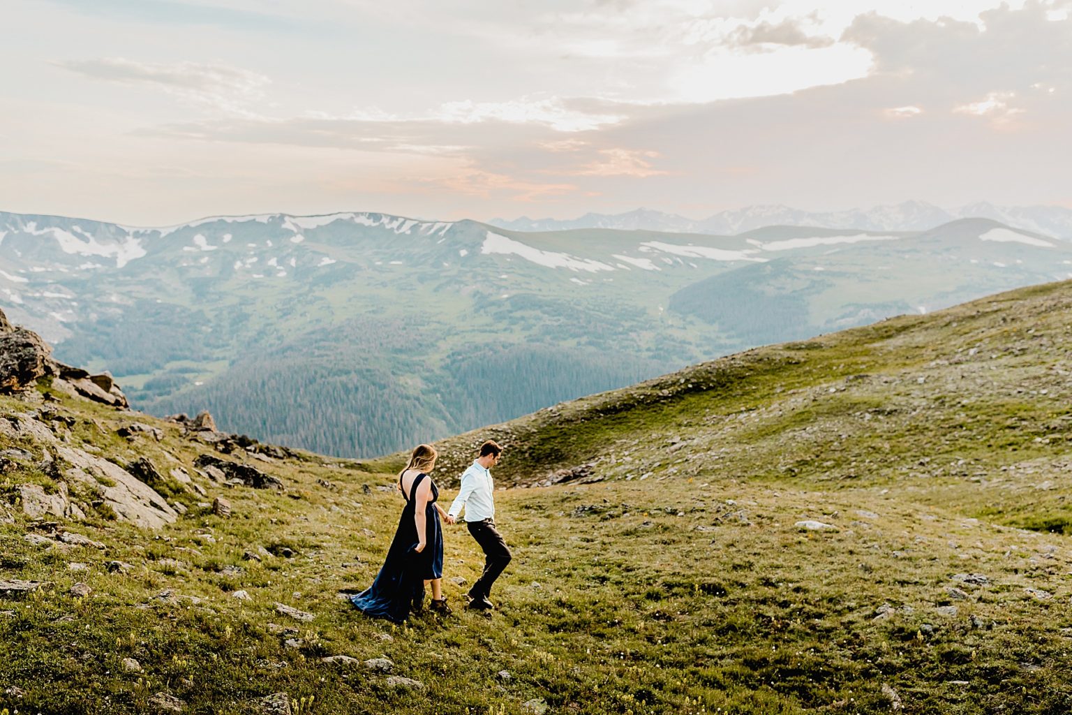 couple hiking down mountain together in their nice attire and hiking shoes with gorgeous mountain backdrop
