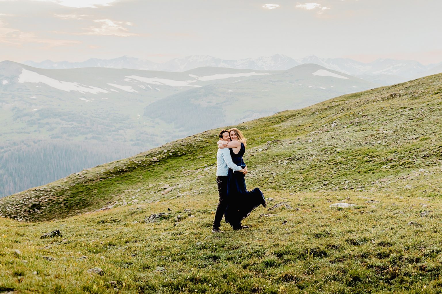 woman gets ready to run into man's arms for a big hug in front of the stunning Rocky Mountains in the green summer grass