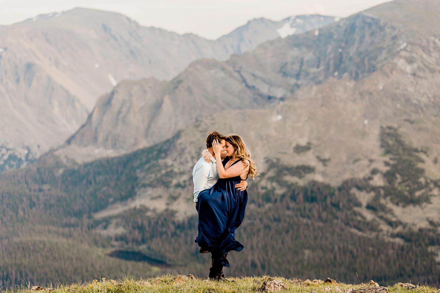couple hugs and embraces with stunning purple and blue Rocky Mountains in the backdrop showing off colorado sunset colors