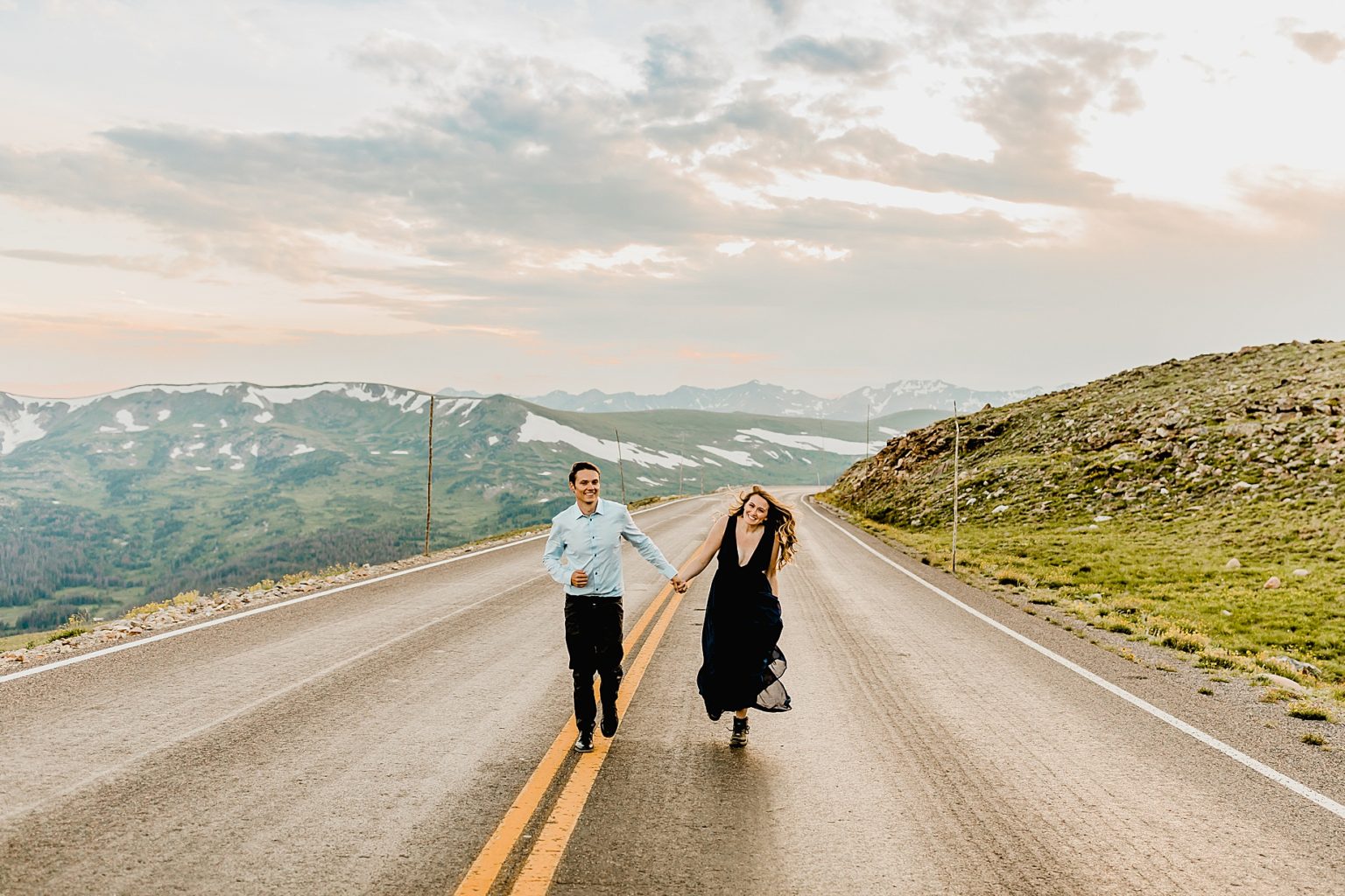 man and woman hold hands running in the street with gorgeous mountain scenery in the background