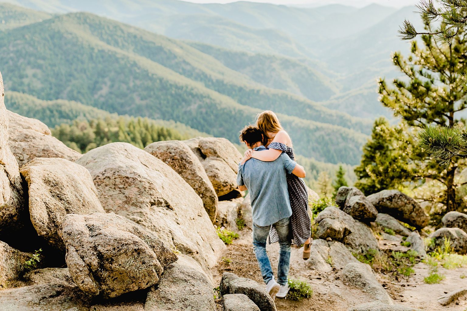 guy lifts girl over rocks with beautiful mountain backdrop