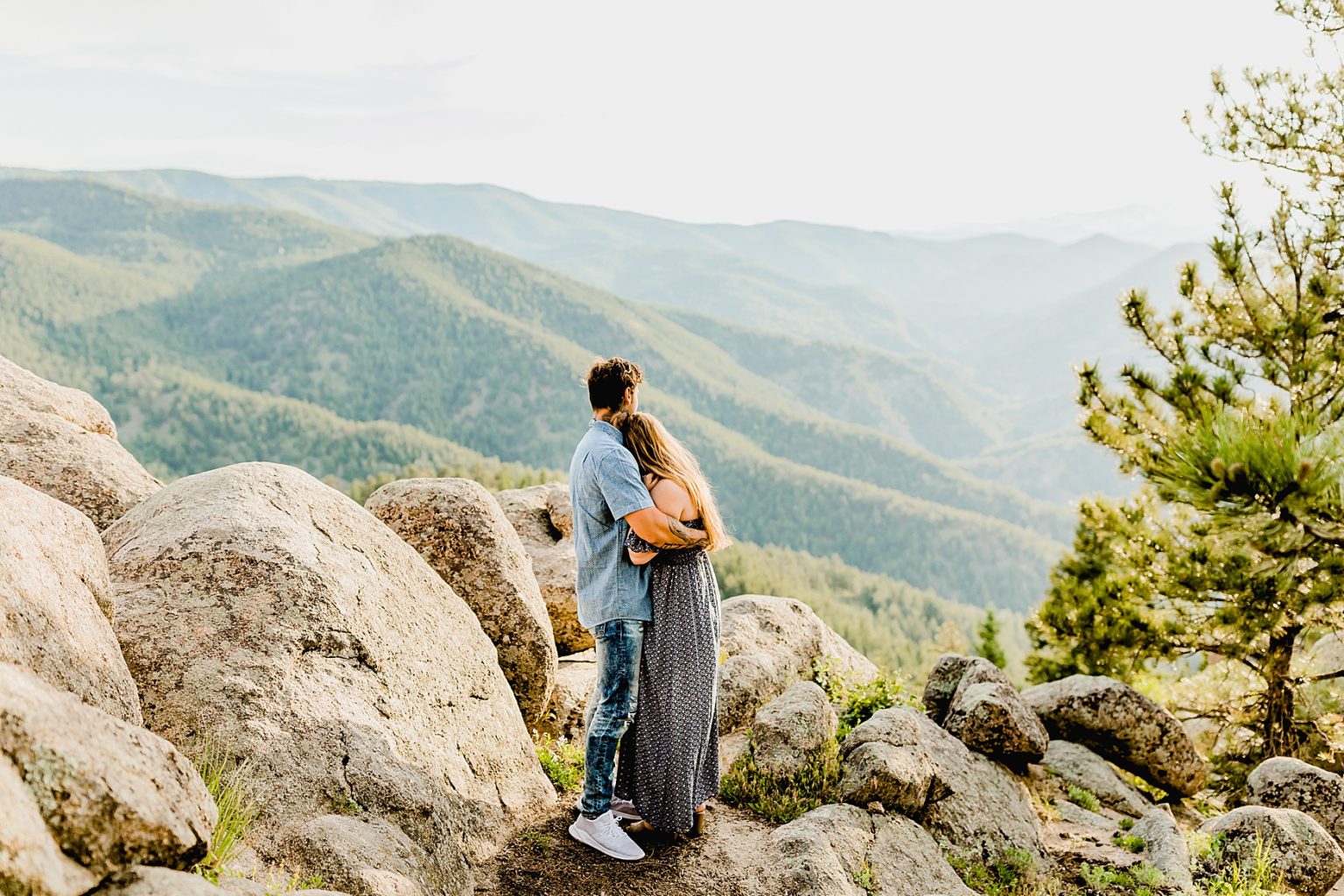 couple embraces with a gorgeous blue mountain backdrop showing off boulder trees and mountains