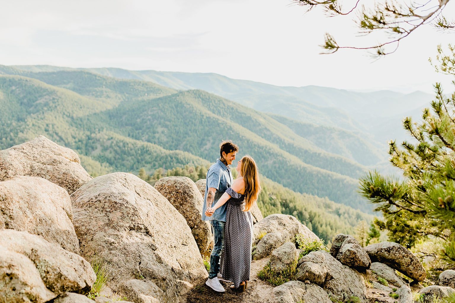 couple embraces with a gorgeous blue mountain backdrop showing off boulder trees and mountains