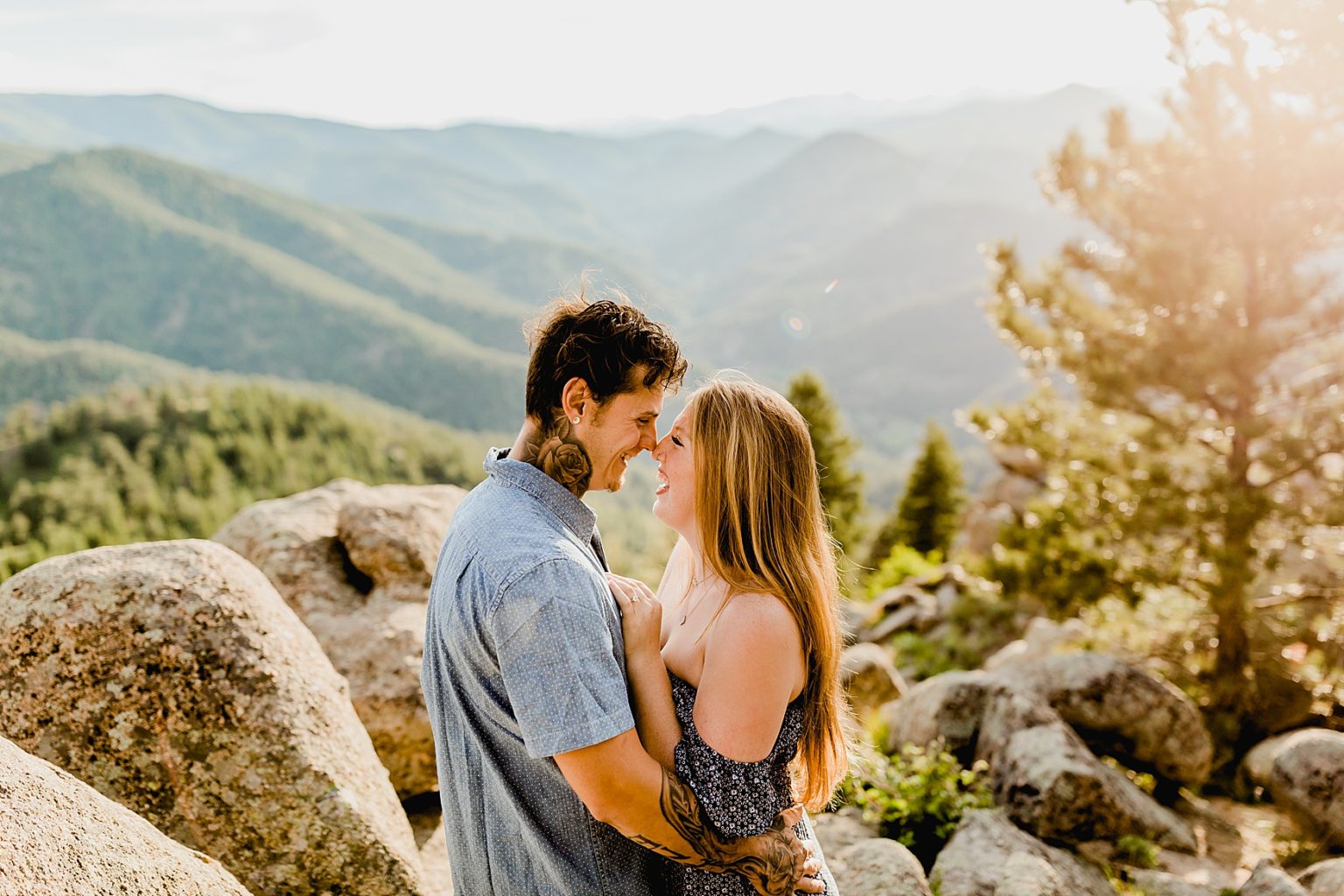 couple laughs together with gorgeous colorado mountain backdrop at sunset surrounded by trees