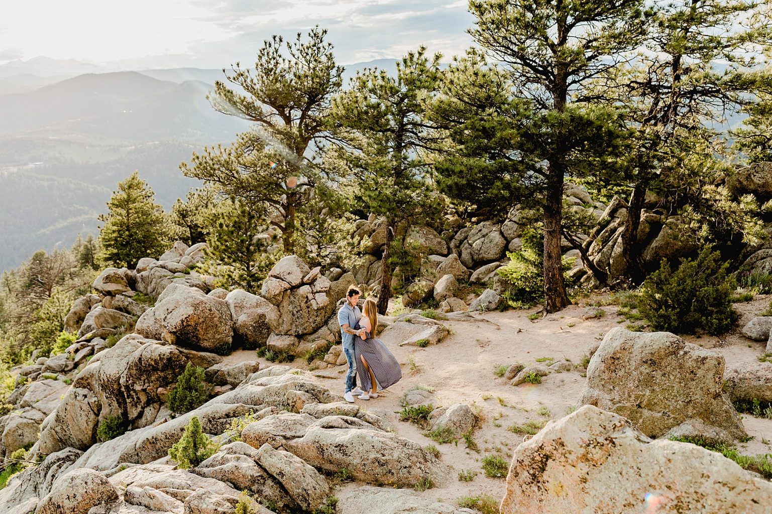 wide angle shot of couple hugging each other with colorado trees, rocks, and mountains in the background