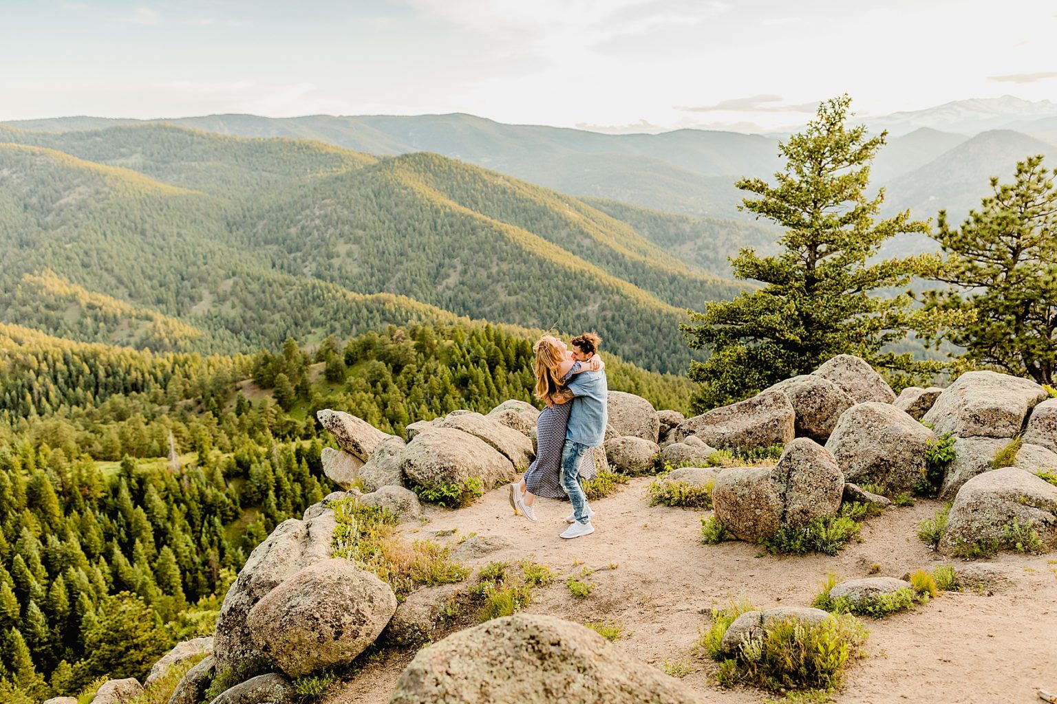 couple holds each other and has a lot of fun while being surrounded by stunning green trees and colorado mountains for adventure engagement photos