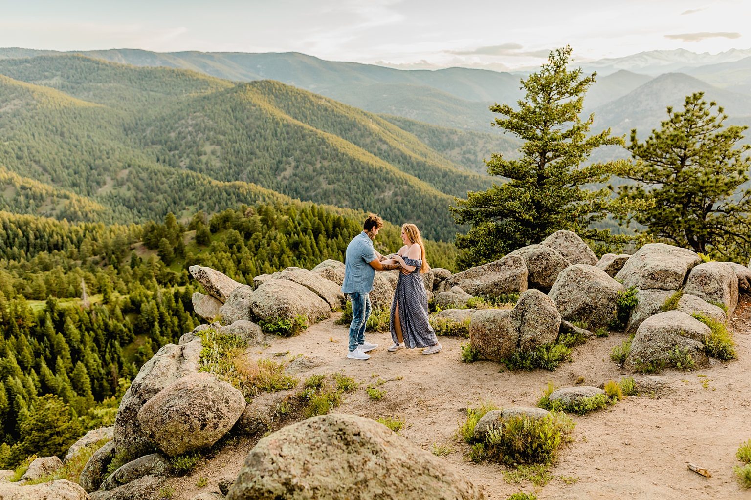 couple tickles each other while being surrounded by stunning green trees and colorado mountains
