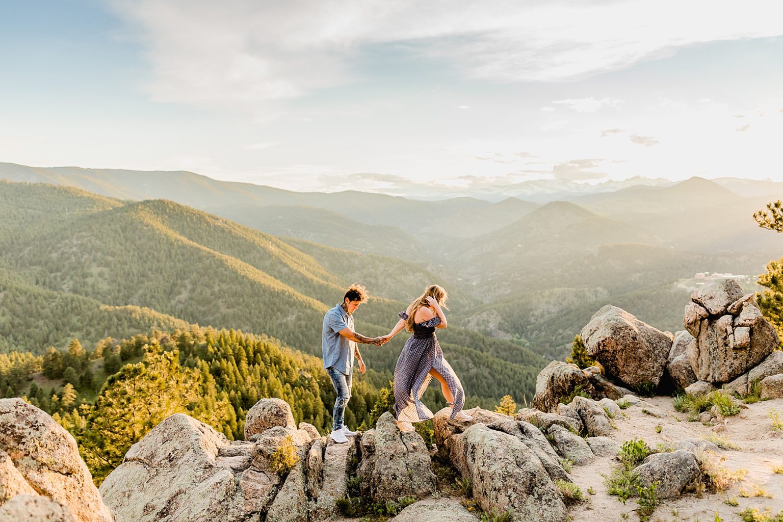 woman leads man as they hold hands and walk together on rock formations with beautiful mountain backdrop for adventure engagement session