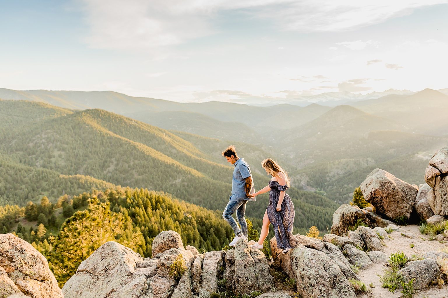 woman leads man as they hold hands and walk together on rock formations with beautiful mountain backdrop for adventure engagement session