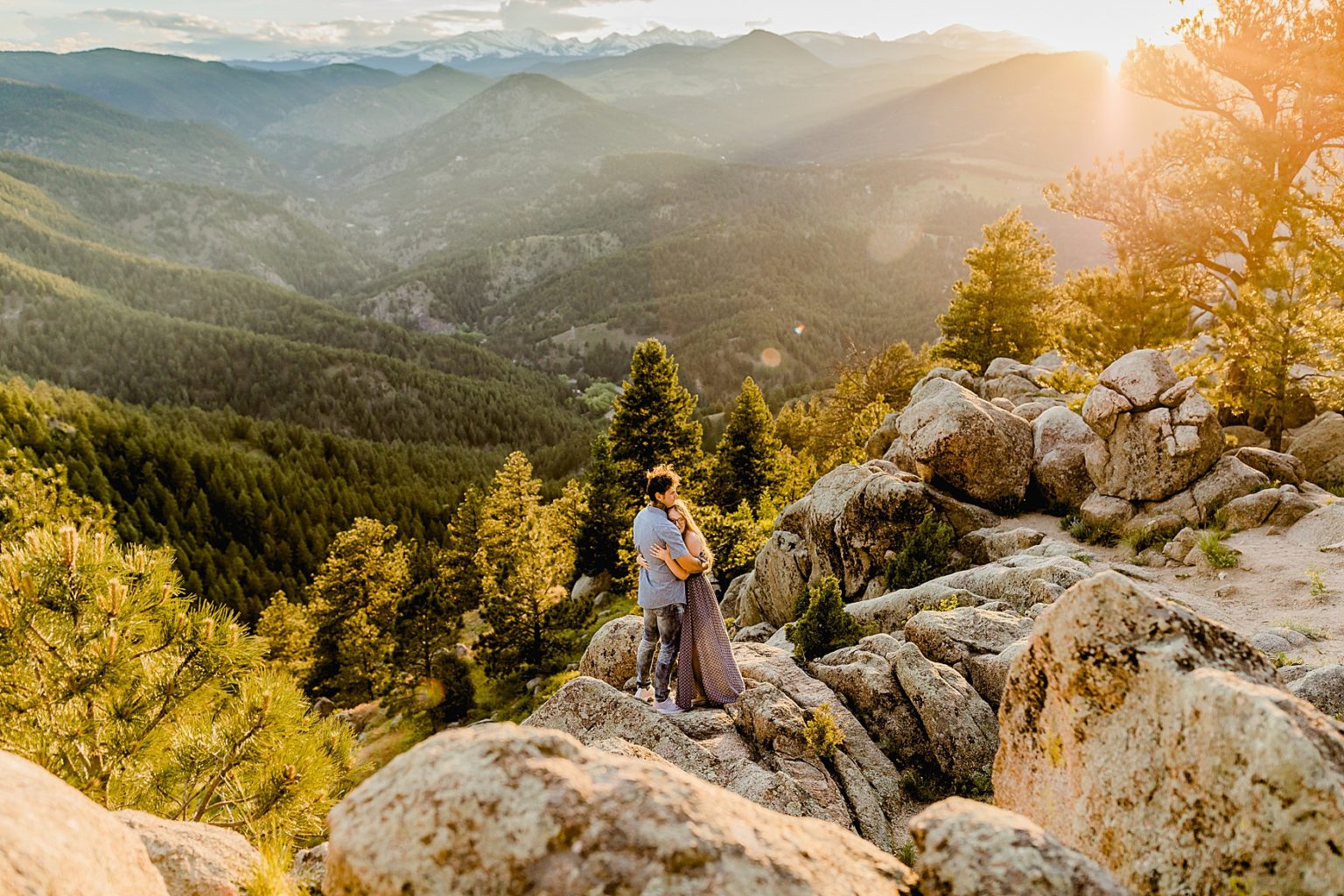 couple stands on rocks hugging each other in boulder colorado with stunning mountain backdrop and an orange sunset