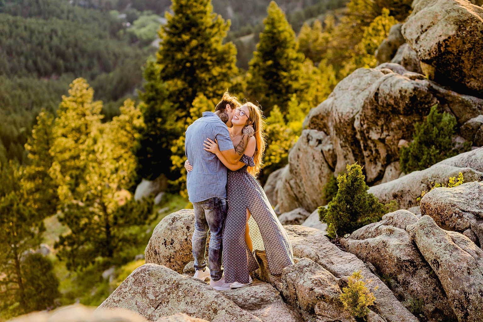 couple stands on rocks hugging each other in boulder colorado with stunning mountain backdrop and an orange sunset