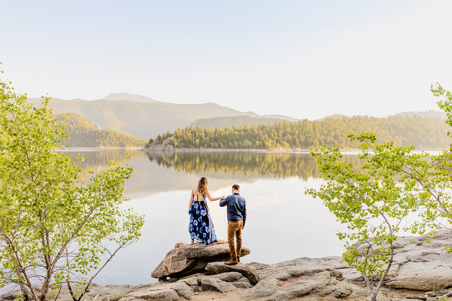 couple stands on rocks in front of beautiful boulder colorado lake with gorgeous mountain scenery