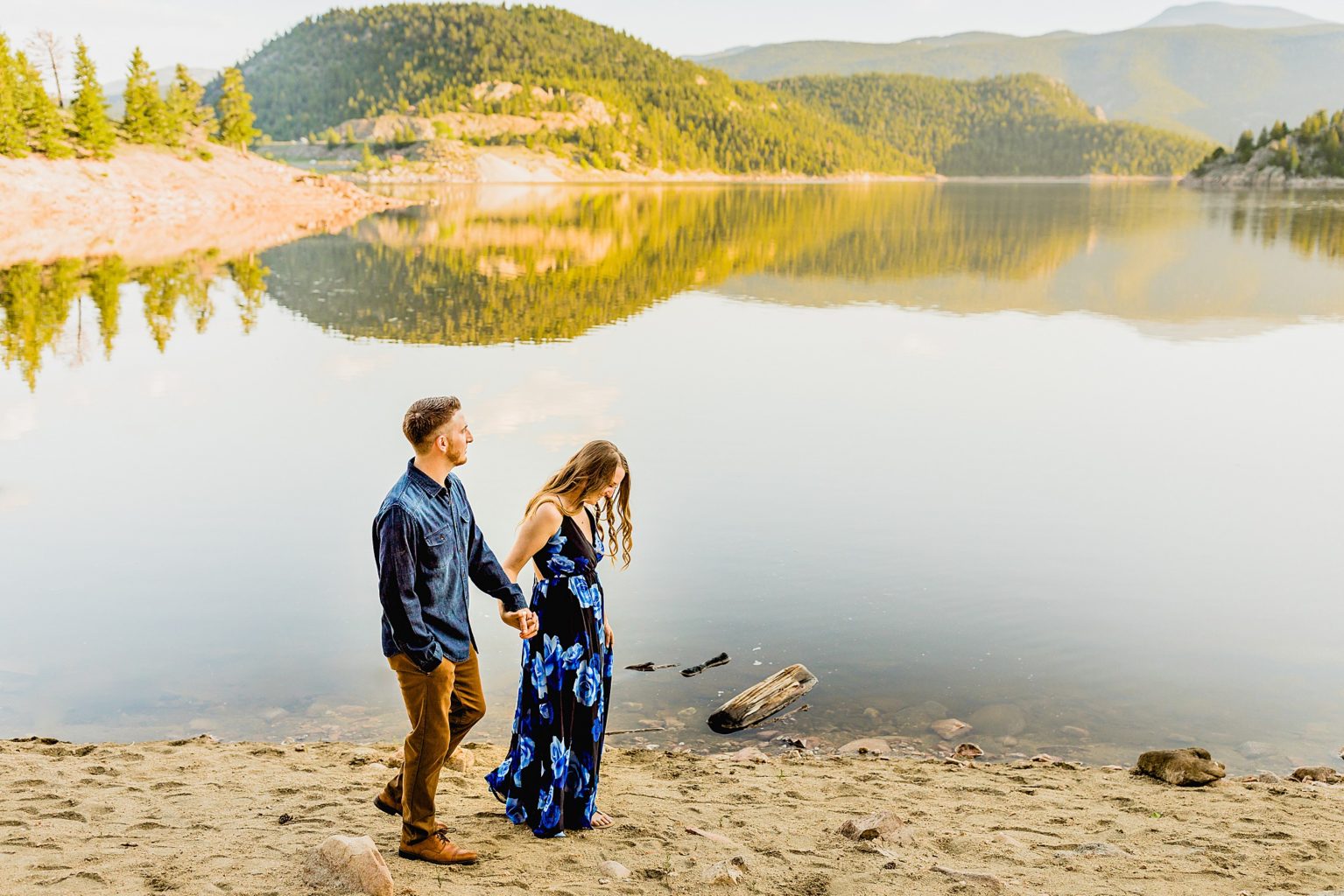 couple holds hands in front of an incredible lake in boulder colorado with stunning rocky mountain backdrop to celebrate anniversary