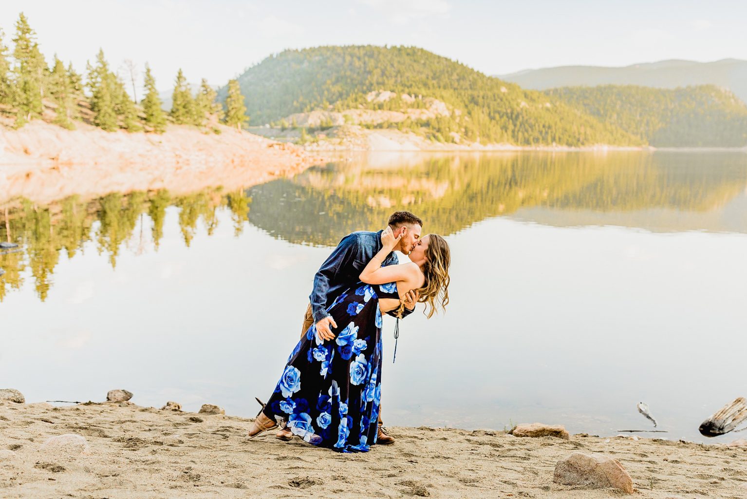 couple holds each other in front of an incredible lake in boulder colorado with stunning rocky mountain backdrop to celebrate anniversary