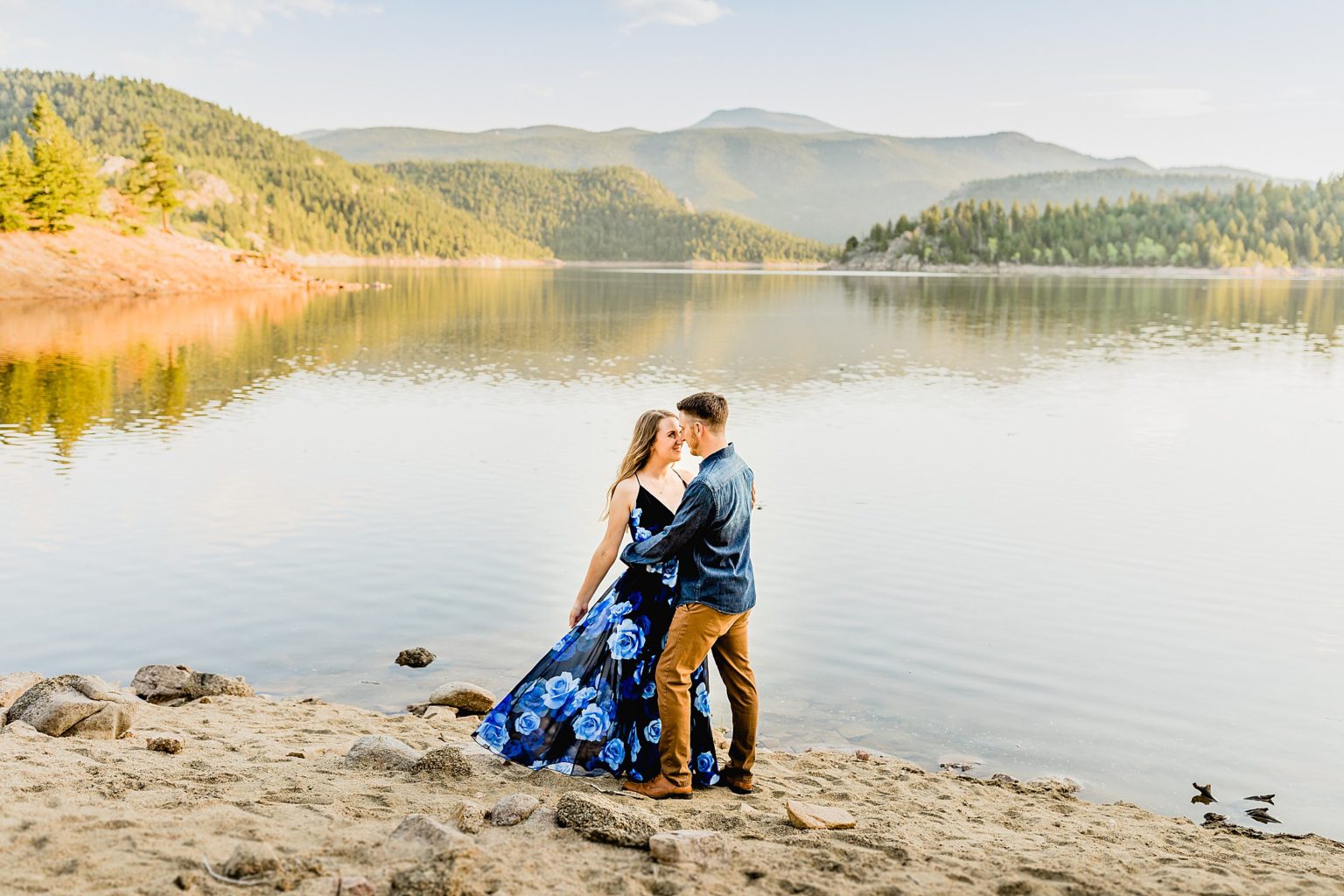 couple holds each other in front of an incredible lake in boulder colorado with stunning rocky mountain backdrop to celebrate anniversary