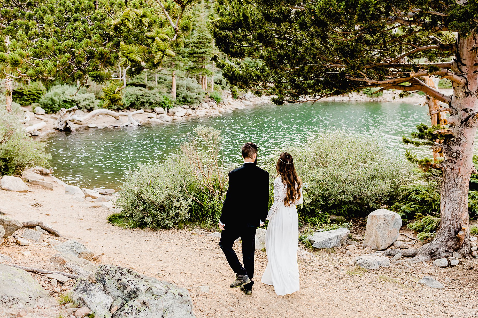 bride and groom walk to elopement location in front of gorgeous blue alpine lake