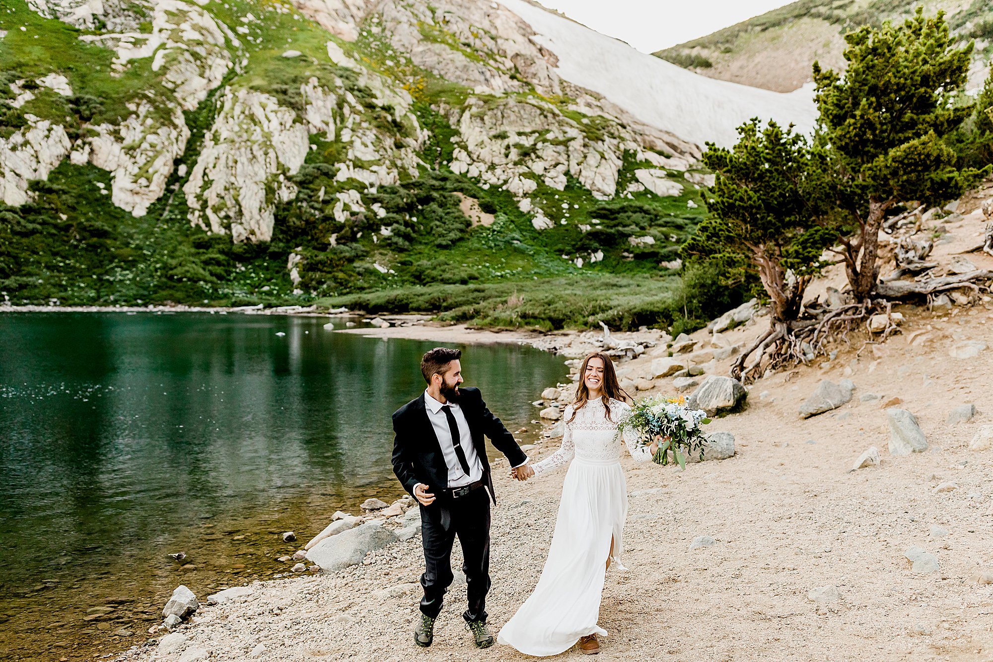 bride and groom run hand in hand next to gorgeous colorado alpine lake for their elopement