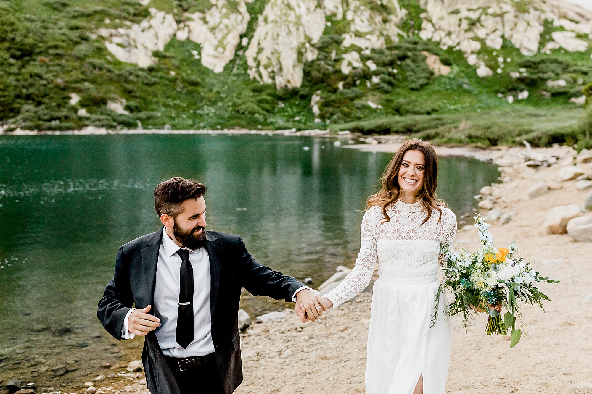 bride and groom run hand in hand next to gorgeous colorado alpine lake for their elopement